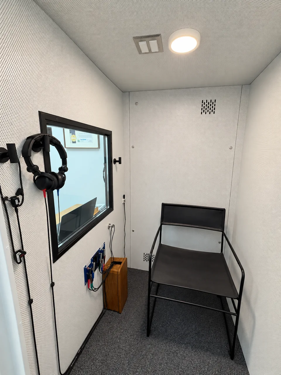 The black patient chair, headphones and observation window inside Pinnacle Audiology’s audiometric booth